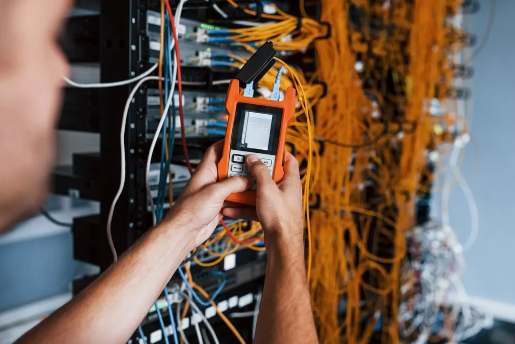 Technician testing a network cable at a patch panel with a handheld certifier